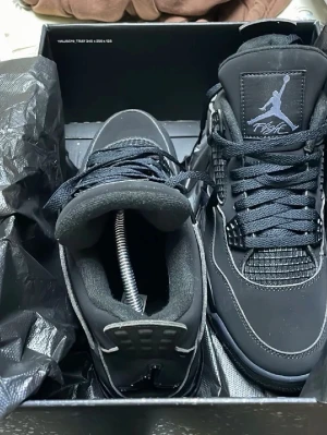 Svarta Blackcats Air Jordan 4 Retro sneakers  - Snygga svarta Air Jordan 4 Retro sneakers med ikoniska Jumpman-loggan på plösen. Skorna har meshdetaljer, svarta skosnören och kontrastsömmar. Ovandelen är i mocka och syntet, och sulan har synlig Air-enhet. Perfekta för dig som gillar streetwear och klassisk sneakerstil.