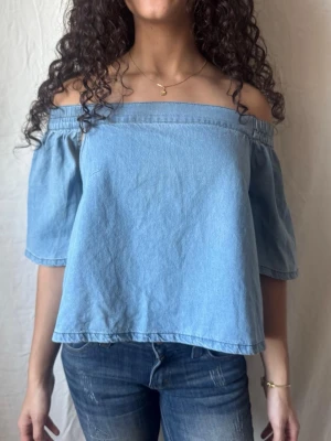 Ljusblå offshoulder denimtopp med öppen rygg - Trendig ljusblå offshoulder topp i denim med korta ärmar och avslappnad passform. Öppen i ryggen med resår. Jätteskönt och mjukt material. Perfekt för en trendig demin look nu till våren eller sommaren. Pris kan diskuteras!🥰