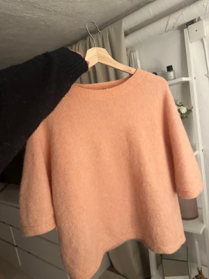 Ljusrosa stickad tröja med 3/4-ärm - Mysig ljusrosa stickad tröja med rund halsringning och trekvartsärmar. Tröjan har en avslappnad passform och är gjord i ett mjukt, fluffigt material som känns skönt mot huden. Perfekt för lager på lager och en chill look.