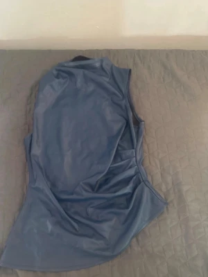 Mörkblå ärmlös korsettopp - Snygg mörkblå korsettopp i syntetmaterial med hög hals och figurnära passform. Toppen är ärmlös och har en stilren, minimalistisk look som passar perfekt till jeans eller kjol.