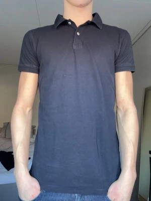 Mörkblå pikétröja med krage - En stilren mörkblå pikétopp med klassisk krage och två knappar framtill. Toppen har korta ärmar och är gjord i mjuk bomull som känns skön mot huden. Passformen är normal och toppen har en enkel, clean look.