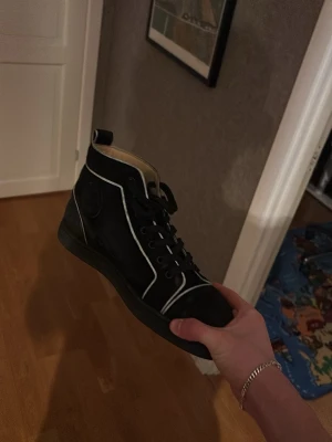 Svarta Louboutin sneakers med vita detaljer - Äkta, använd några gånger, Svarta sneakers från Christian Louboutin i mocka med vita kontrastdetaljer och klassisk logga på sidan. PRIS KAN ABSOLUT DISKUTERAS. 