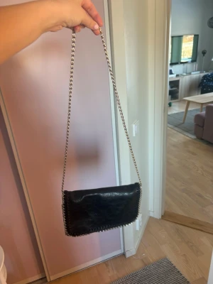 Svart axelremsväska med kedja ! 🖤 - Snygg svart handväska i skinnimitation med silverfärgad kedjerem. Väskan har dekorativa sömmar längs kanterna och en mjuk, lite slouchy form. Perfekt storlek för det viktigaste och ger en cool touch till din outfit.
