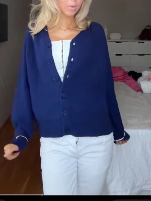 Mörkblå stickad kofta med knappar - Snygg mörkblå stickad kofta med v-ringning och stora knappar framtill. Koftan har en loose passform och långa ärmar, perfekt att slänga över en topp för en chill look.