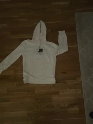 Vit hoodie från Dolce & Gabbana - Snygg vit hoodie från Dolce & Gabbana med exklusiv metallbricka framtill och justerbar huva med metalländar på snörena. Tillverkad i mjukt tyg som känns skönt mot huden. Perfekt för dig som vill ha en stilren och lyxig look.