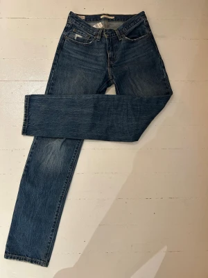Mörkblå Levi’s Middy Straight jeans - Säljer ett par klassiska blå jeans från Levi's, modell Middy Straight. Jeansen har rak passform, fem fickor och snygga slitningar vid fickorna. Tillverkade i slitstarkt denimtyg i 100% bomull med kontrastsömmar och dragkedjegylf. 