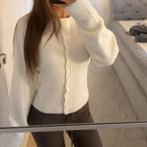 Vit stickad tröja - Mjuk fin tröja med knappar som kan öppnas, ribbad längst ner i midjan och nere vid ärmarna.