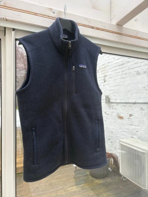  Patagonia väst - Klassisk mörkblå fleeceväst från Patagonia med hög krage och hel dragkedja framtill. Västen har två sidofickor med dragkedja och en bröstficka med dragkedja. Perfekt lager för kyliga dagar och enkel att matcha med olika outfits.STORLEK S. Knappt använd. 