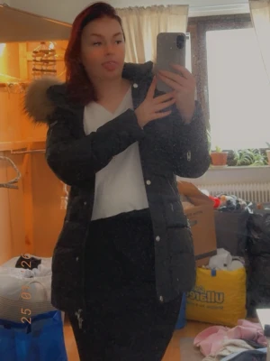 Svart dunjacka med pälsdetalj - Säljer en svart dunjacka med quiltad design och pälsdetalj på huvan. Jackan har flera dragkedjor, knappar och en normal passform. Perfekt för kalla dagar och har en snygg, modern look.