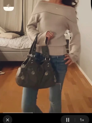 Beige off shoulder stickad tröja - Trendig beige stickad tröja med off shoulder-design och bred ribbad mudd i midjan och vid ärmsluten. Tröjan har en avslappnad passform och långa ärmar, perfekt för en snygg och bekväm look.