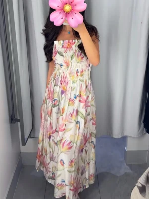 Blommig långklänning - Säljer en superfin långklänning med blommigt mönster i pastellfärger och små fåglar. Klänningen har smock upptill, tunna axelband och en luftig, flowy kjol. Perfekt för varma dagar och ger en romantisk vibe.