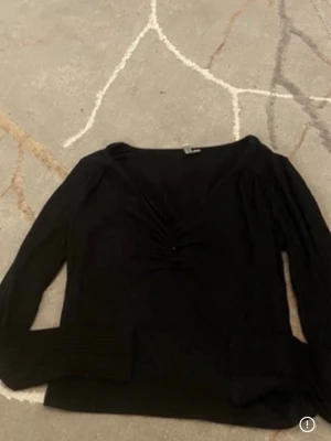 Svart långärmad topp med rynk - Snygg svart långärmad topp med v-ringning och rynkdetalj framtill. Toppen har en smickrande passform och är perfekt att styla till jeans eller kjol. Materialet känns mjukt och stretchigt.