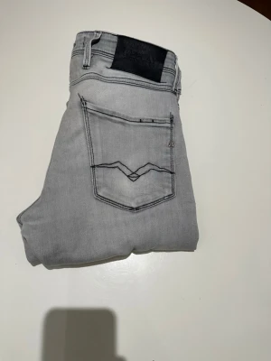 Ljusgrå slim fit jeans från Replay - Snygga ljusgrå jeans från Replay med slim fit-passform. Jeansen har klassiska fem fickor, svarta detaljer och coola sömmar på bakfickan. Perfekta för dig som gillar en modern och stilren look. Modellen är 187 och väger 70 kg. Vid funderingar är det bara att skriva!