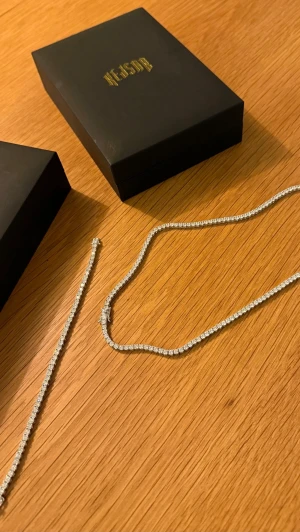 Tennis Halsband och Armband - Hej! Säljer ett elegant Tennis halsband 3 mm bred och 50 cm lång, tillsammans med ett matchande Tennis armband 3 mm bred och 17.5 cm lång. Smyckena medföljs med lyxiga smyckeslådor. Båda smyckena är köpta ifrån Kejsar.se med hög kvalité, endast använts ett fåtal gånger. Paketpris för båda smyckena 1499 kr, endast halsbandet 899 kr och endast armbandet 799 kr. Hör av er vid intresse!