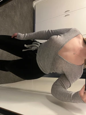 Grå omlottopp - Snygg grå omlottopp med djup v-ringning och långa ärmar. Toppen har ett knyt i midjan som ger en feminin siluett. Perfekt till vardags eller söt till träning🩶