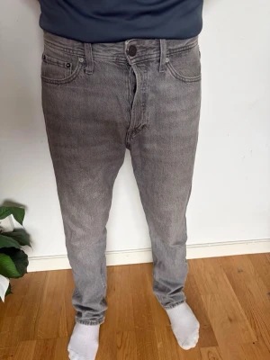 Grå raka jeans från Jack n jones - Säljer ett par grå jeans från Jack n jones med klassisk femficksdesign och raka ben. Jeansen har en snygg tvättad look och är tillverkade i bomull. Perfekta för en avslappnad stil och passar till det mesta.