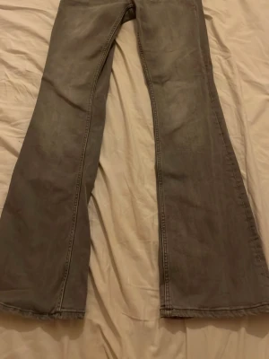 Gråa utsvängda jeans - Säljer ett par gråa jeans med utsvängda ben och klassisk femficksdesign. Jeansen har en snygg vintagekänsla och är perfekta för dig som gillar retrostil. Materialet är denim och passformen är relaxed med extra vidd nedtill.