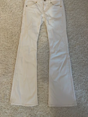 Vita bootcut jeans med fickdetalj - Vita bootcut jeans med guldiga detaljer. Jeansen har utsvängda ben och materialet är denim i bomull.