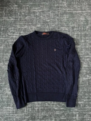 Mörkblå kabelstickad tröja Morris - Snygg mörkblå kabelstickad tröja från Morris i 100% merinoull. Tröjan har rund halsringning, långa ärmar och en liten broderad logga på bröstet. Perfekt för dig som gillar klassisk och stilren look.