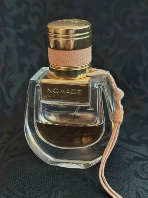 Chloé Nomade Eau de Parfum 30 ml  - Chloé Nomade Eau de Parfum i en elegant glasflaska med gulddetaljer och beige mockaband. Flaskan har en unik, rundad form och locket är dekorerat med både guld och mocka. Doften är modern och feminin, perfekt för dig som gillar lyxiga parfymer.