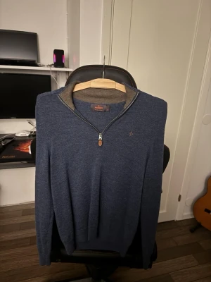 Blå merinoulltröja från Morris - Snygg blå tröja från Morris i 100% merinoull. Tröjan har halv dragkedja med läderdetalj, ribbad krage i kontrastfärg och diskret Morris-logga broderad på bröstet. Perfekt för dig som gillar stilrena och bekväma plagg. Använd enstaka gånger o är en riktigt brudmagnet;)