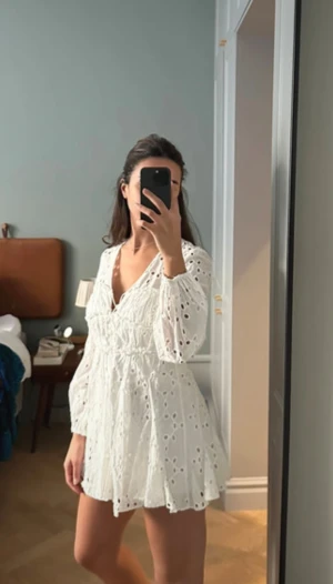 Vit kort klänning med spetsdetaljer - Superfin vit kort klänning med v-ringning och långa ärmar. Klänningen har broderade spetsdetaljer. Är i stl S