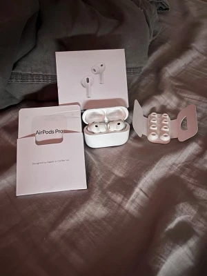 Apple AirPods Pro med laddningsetui - Säljer ett par vita Apple AirPods Pro med trådlöst laddningsetui. Hörlurarna har silikonproppar i olika storlekar och levereras med originalförpackning och manual. Snygg och kompakt design i blankt plastmaterial, perfekt för dig som vill ha grymt ljud och smidig användning.