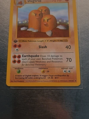 Dugtrio 1st Edition  - Säljer ett Dugtrio Pokémonkort från Base Set 1999. Kortet har gul ram, motiv av tre bruna Dugtrio och är på engelska. Kortet har attackerna Slash och Earthquake och är nummer 19/102. Perfekt för samlare eller Pokémonfans!