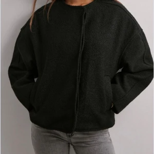 Svart oversized cardiganjacka - Svart cardiganjacka i oversized modell med knappar framtill och två fickor. Jackan har en rak passform och är tillverkad i ett mjukt, strukturerat material som ger en cool och avslappnad look. Perfekt att slänga över en t-shirt eller hoodie.