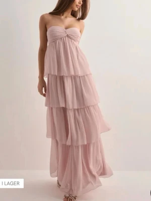 Ljusrosa långklänning med volanger - Säljer min otroliga balklänning från Nelly! Dreamy frill dress i färgen light pink, Storlek XS. SLUTSÅLD Ljusrosa långklänning med flera lager volanger och axelbandslös design. Klänningen har en söt twistad detalj vid bysten och faller mjukt i ett luftigt tyg, perfekt för sommarens alla tillfällen.