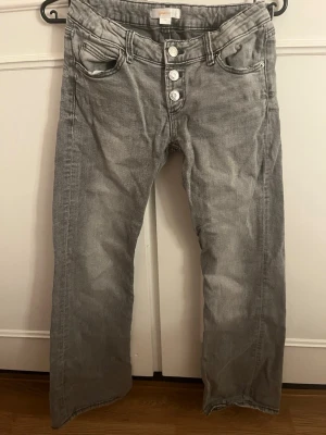 Grå raka jeans med knappar - Snygga grå jeans med utsvängda ben och tre synliga knappar framtill. Klassisk femficksmodell och cool tvättad look. Perfekta för en avslappnad stil och lätta att matcha med olika toppar.