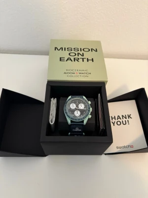 Omega x Swatch MoonSwatch grön - Säljer en Omega x Swatch MoonSwatch Mission on Earth med grön boett och svart urtavla. Klockan har vita detaljer och flera subdials. Tillverkad i biokeramik, stilren klocka. 💫