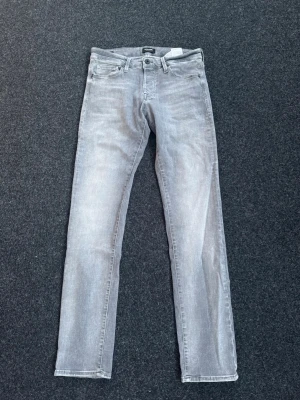 Grå slim fit jeans från Jack & Jones - Snygga grå slim fit jeans från Jack & Jones med klassisk femficksdesign och diskreta slitningar. Jeansen har normal midja, raka ben och är tillverkade i ett mjukt denimtyg med lite stretch för extra komfort.      W31-L32
