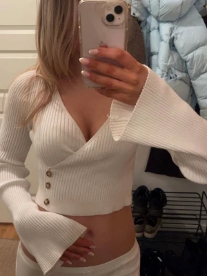 Vit ribbad omlottopp - Supersöt krämvit omlotttopp från na-kd med djup v-ringning, utsvängda ärmar och detalj med knappar. Tillverkat i ett ribbat mjukt tyg med stretch som ger en jätteskön känsla. Perfekt för dig som gillar stilrena och moderna plagg! 