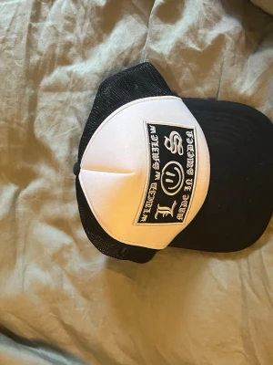 Svart vit keps från chrome hearts - Säljer en svartvit chrome hearts keps med mesh på sidorna och bak. Kepsen har böjd skärm och justerbar snapback. Perfekt för dig som gillar streetwear och unik stil. Inte använd mycket alls!