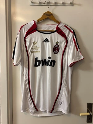 AC Milan KAKA tröja - Säljer en vit AC Milan matchtröja från Adidas med Champions League-detaljer och Bwin som sponsor. Tröjan har röda och svarta detaljer, klubbmärke på bröstet och broderad stjärna. Perfekt för dig som älskar fotboll och vill ha en ikonisk supportertröja.