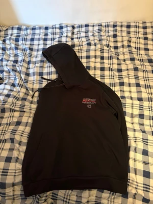 Svart hoodie McKenzie med huva - Svart hoodie från McKenzi med broderad logga och text på bröstet samt siffran 92. Klassisk känguruficka framtill och justerbar huva med snören. Perfekt för en avslappnad streetwear-look. Hoodie är xs