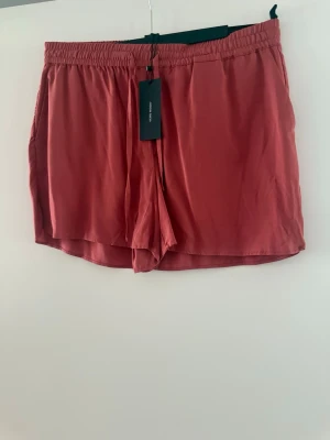 Rostrosa shorts från Vero Moda strl L - Säljer ett par rostrosa shorts med elastisk midja och avslappnad passform. Tillverkade i ett mjukt och lätt material som passar perfekt för varma dagar. Enkla att matcha och riktigt sköna att bära.
