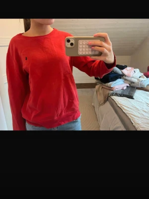 Röd sweatshirt från Ralph Lauren - Säljer en klassisk röd sweatshirt från Ralph Lauren med rund halsringning och diskret broderad logga på bröstet. Tröjan har en avslappnad passform. Den är i storlek L fast barnstorlek så skulle säga att den passar en storlek s.