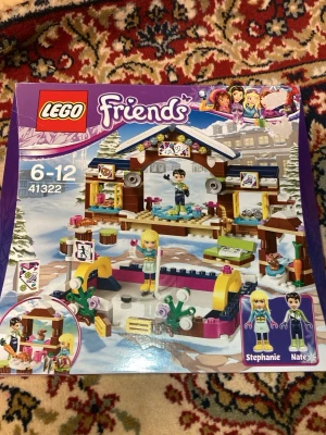 LEGO Friends Vinterresort 41322 - Säljer ett LEGO Friends set, modell 41322 Vinterresort. Setet innehåller färgglada byggklossar i plast, vintertema med isbana, stuga och tillbehör samt minifigurerna Stephanie och Nate. Passar för dig som gillar att bygga och skapa egna vinteräventyr.