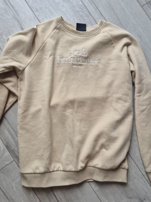 Beige sweatshirt Peak Performance - Beige sweatshirt från Peak Performance med broderad logga på bröstet. Tröjan har rundad hals, ribbade muddar vid ärmslut och nederkant samt en relaxed fit. Tillverkad i mjukt bomullsmaterial som känns skönt mot huden.