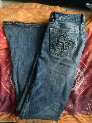 Blå jeans med broderade bakfickor - Snygga blå jeans med raka ben och coola broderade detaljer på båda bakfickorna. Jeansen har klassisk femficksdesign och är tillverkade i denim. Perfekta för dig som vill sticka ut lite extra med detaljer på fickorna. Midjemått är 32 cm