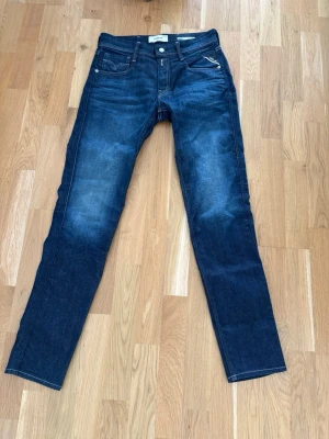 Mörkblå Anbass jeans Replay - Helt nya mörkblå jeans från REPLAY, modell Anbass med slim fit passform. Storlek 29x32 med mått enligt bild. Jeansen är endast använda 1 gång, därav klassar jag de som nyskick, utan några skavanker eller defekter.