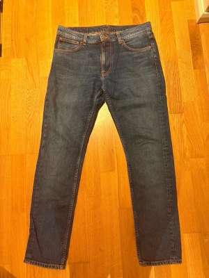 Blå raka jeans från Nudie Jeans, modell lean dean, 32L 32W - Säljer ett par klassiska blå jeans från Nudie Jeans med rak passform och snygga kontrastsömmar. Jeansen är modellen lean Dean 32L 32W. Tillverkade i slitstark denim, perfekta för en avslappnad stil.
