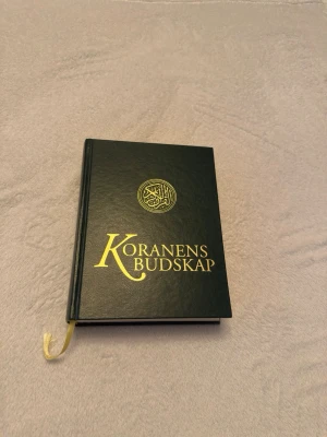 Koranens Budskap med översättning på svenska  - Koranens Budskap är en svart hårdbunden bok med guldfärgad text och symbol på omslaget. Boken har ett inbyggt bokmärke i gult band och är utgiven av Sakma. Perfekt för dig som vill läsa och utforska Koranens budskap på svenska. Översättning av Muhammed Knutsson