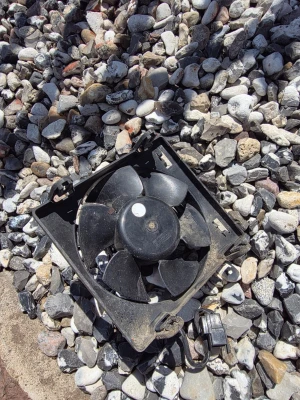 Svart kylfläkt derbi - En svart kylfläkt i plast med fem blad och fyrkantig ram. Fläkten har en anslutningskabel med kontakt och är troligen avsedd för elektronik eller fordon. Passar för dig som behöver extra kylning till dator, elektronik eller bil.