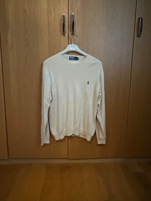 Beige tröja från Polo Ralph Lauren - Klassisk beige tröja från Polo Ralph Lauren med rund halsringning och material i bomull. Tröjan har använts sparsamt, och skicket = 8,5/10. Det finns inga defekter. 