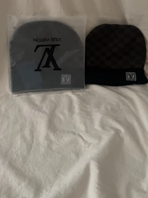 Grå mössa från Louis Vuitton - Snygg grå mössa från Louis Vuitton med klassiskt LV-monogram och diskret rutmönster. Mössan är stilren och passar perfekt till höstens och vinterns outfits. Kommer i originalförpackning med tagg kvar.