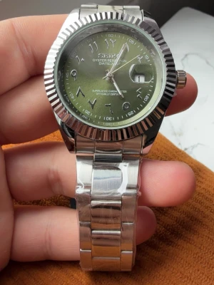 Grön klocka med silverlänk -  klocka med grön urtavla och arabiska siffror. Klockan har en robust silverfärgad länk i metall och räfflad bezel. Urtavlan har datumfönster och tydliga visare. Perfekt accessoar för dig som gillar klassisk men unik stil.