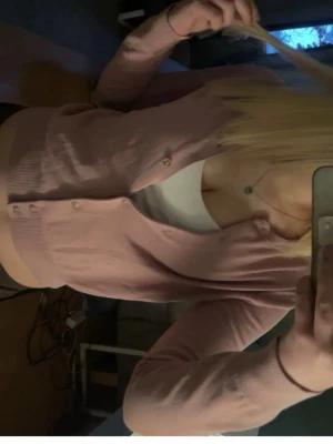 Ljusrosa cardigan med knappar - Söt ljusrosa cardigan med rund halsringning och knäppning framtill. Tröjan har långa ärmar och ribbade muddar vid ärmslut och nederkant. Perfekt att slänga över ett linne eller t-shirt för en chill look.
